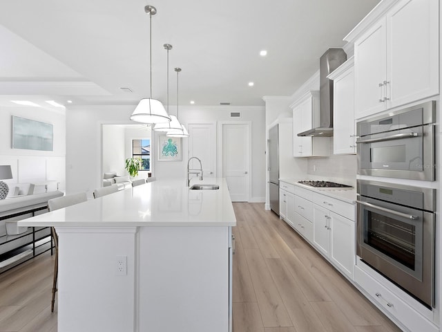 kitchen featuring crown molding, white cabinets, a sink, and wall chimney range hood