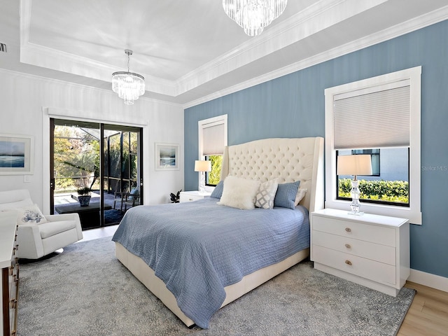 bedroom featuring an inviting chandelier, access to exterior, a tray ceiling, ornamental molding, and light hardwood / wood-style floors