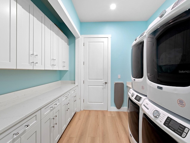 laundry area with light hardwood / wood-style flooring, cabinets, and stacked washer / dryer