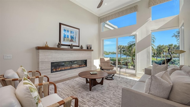 living room featuring a towering ceiling, wood-type flooring, crown molding, ceiling fan, and a premium fireplace