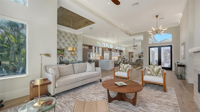 living room with a towering ceiling, a wealth of natural light, ornamental molding, and light wood-type flooring