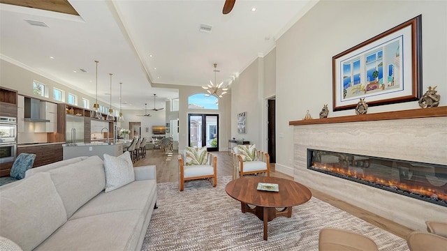 living room with sink, crown molding, a premium fireplace, a high ceiling, and light wood-type flooring