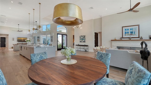 dining space with ceiling fan, ornamental molding, light hardwood / wood-style floors, and a high ceiling