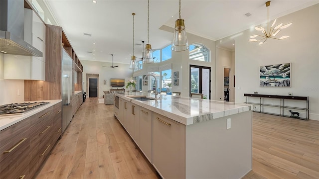 kitchen featuring white cabinetry, sink, a large island with sink, light stone countertops, and wall chimney exhaust hood