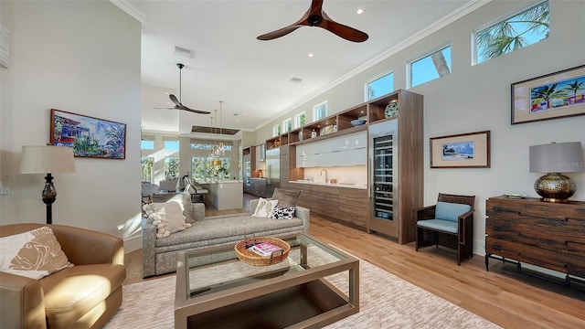 living room with crown molding, a towering ceiling, ceiling fan, and light hardwood / wood-style floors