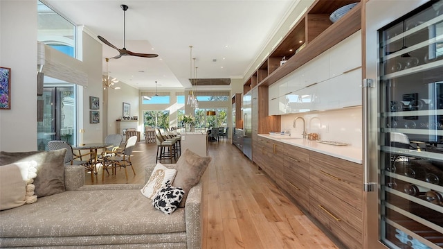 interior space with wine cooler, sink, white cabinetry, light wood-type flooring, and pendant lighting