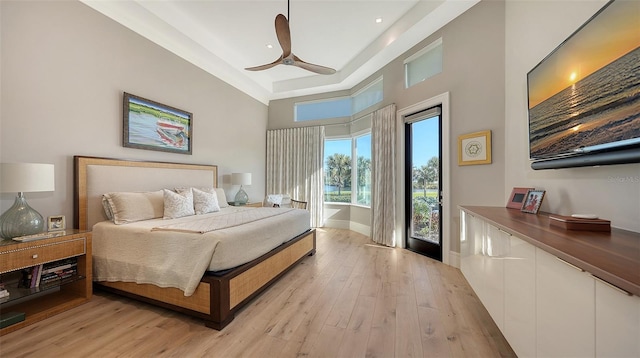 bedroom with ceiling fan, a tray ceiling, light hardwood / wood-style floors, and access to outside