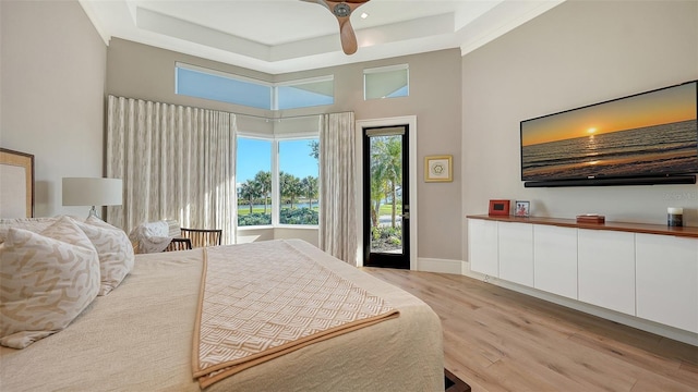 bedroom featuring ceiling fan, a high ceiling, light hardwood / wood-style floors, access to outside, and a raised ceiling