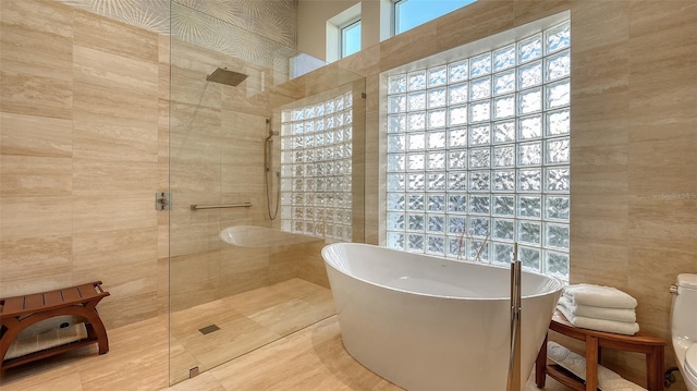 bathroom with tile walls, shower with separate bathtub, and toilet