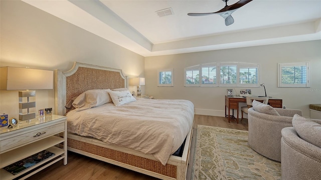 bedroom with wood-type flooring, a raised ceiling, and ceiling fan