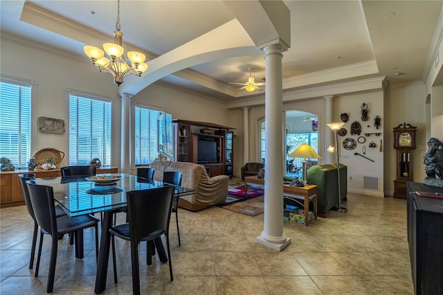 tiled dining room with ornamental molding, a tray ceiling, ceiling fan with notable chandelier, and ornate columns