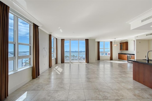 unfurnished living room with sink, a water view, light tile patterned floors, ornamental molding, and a wall of windows