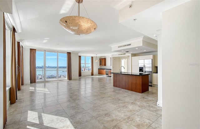 kitchen featuring pendant lighting, sink, stainless steel fridge, a wall of windows, and a water view