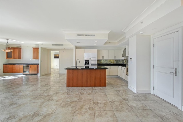 kitchen featuring appliances with stainless steel finishes, tasteful backsplash, white cabinets, a center island with sink, and beverage cooler