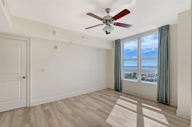 empty room featuring light hardwood / wood-style flooring, ceiling fan, and a water view