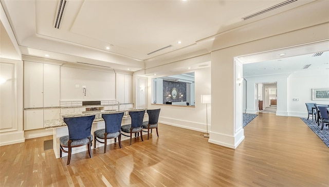 kitchen with a breakfast bar, light stone counters, white cabinets, light wood-type flooring, and ornate columns