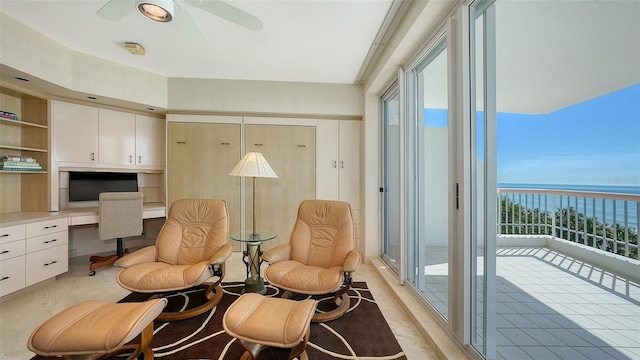 sitting room with a water view, plenty of natural light, built in desk, and ceiling fan