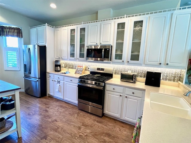 kitchen featuring light wood-type flooring, stainless steel appliances, sink, backsplash, and white cabinets