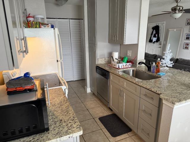 kitchen with sink, white fridge, stainless steel dishwasher, light tile patterned floors, and light stone counters