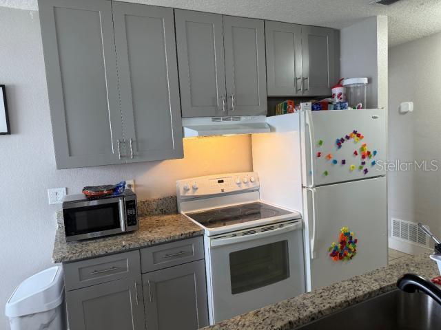 kitchen with white appliances, gray cabinets, a textured ceiling, and stone counters