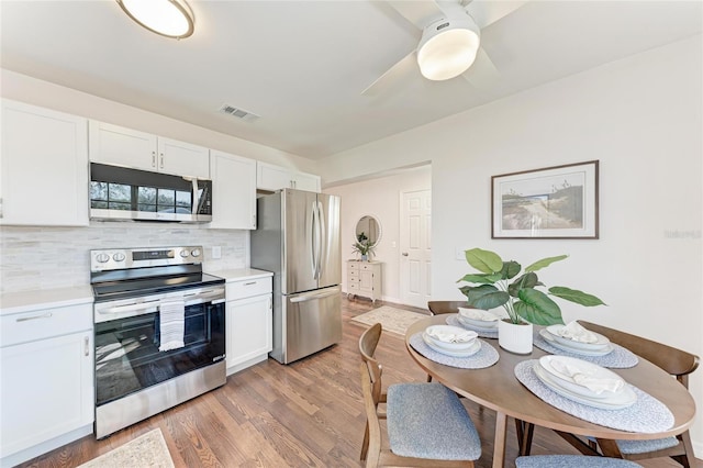 kitchen with appliances with stainless steel finishes, wood-type flooring, white cabinets, decorative backsplash, and ceiling fan