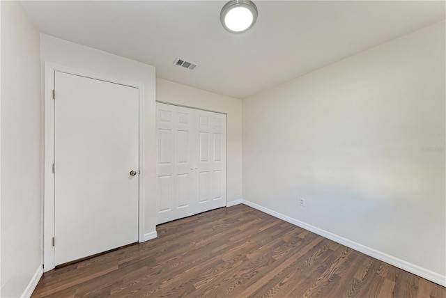 unfurnished bedroom with dark wood-style floors, a closet, visible vents, and baseboards