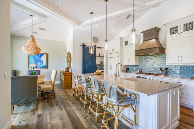 kitchen with custom exhaust hood, white cabinetry, a barn door, and decorative light fixtures