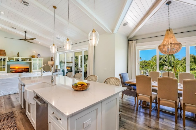 kitchen featuring a center island with sink, vaulted ceiling with beams, pendant lighting, and white cabinets