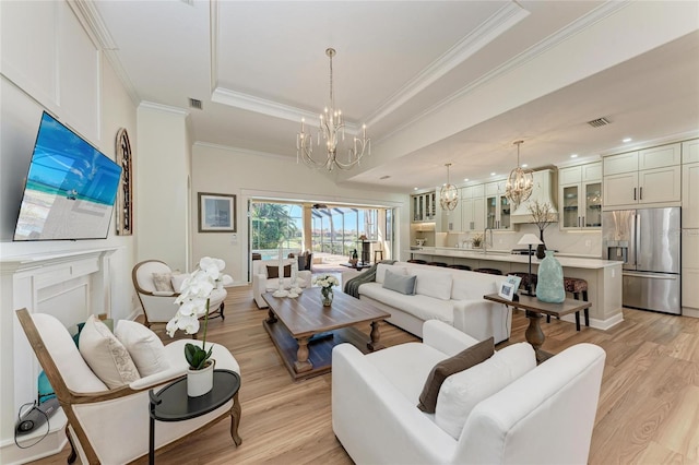 living room with sink, light hardwood / wood-style floors, a tray ceiling, crown molding, and an inviting chandelier