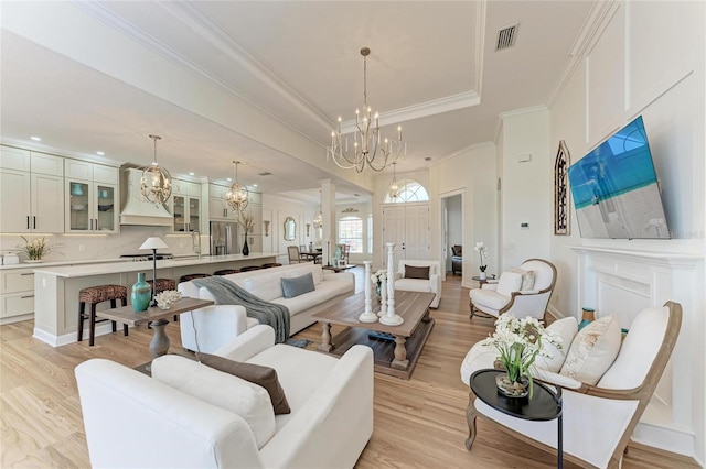 living room with decorative columns, a chandelier, light hardwood / wood-style floors, and a raised ceiling