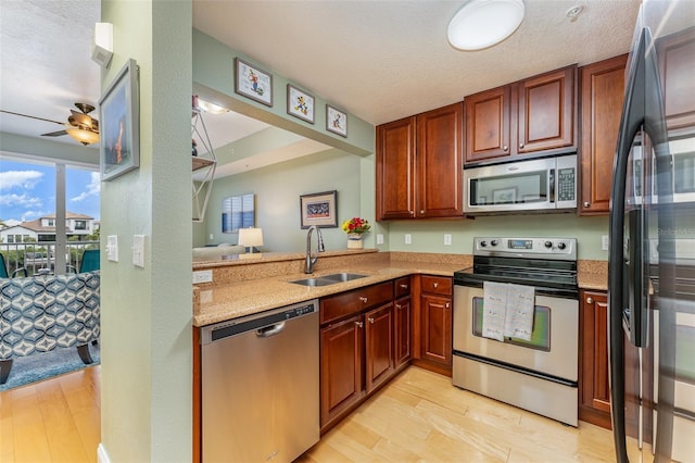 kitchen featuring sink, a textured ceiling, light wood-type flooring, kitchen peninsula, and stainless steel appliances