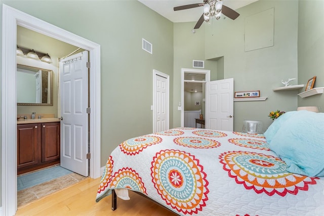 bedroom featuring connected bathroom, high vaulted ceiling, sink, ceiling fan, and light hardwood / wood-style flooring