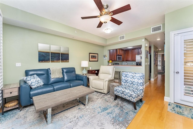 living room featuring light wood-type flooring, baseboards, a ceiling fan, and visible vents