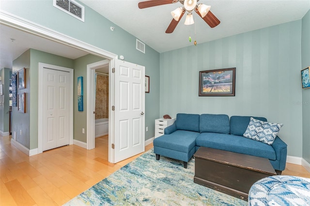 living area featuring ceiling fan, light wood finished floors, baseboards, and visible vents