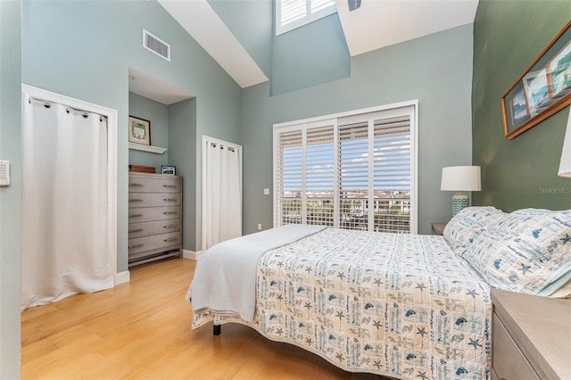 bedroom with wood finished floors, a high ceiling, multiple windows, and visible vents