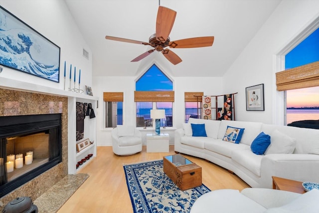 living room featuring a premium fireplace, lofted ceiling, ceiling fan, and light hardwood / wood-style floors