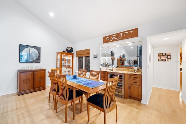 dining space with indoor bar, high vaulted ceiling, wine cooler, and light hardwood / wood-style floors