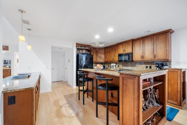 kitchen featuring decorative backsplash, hanging light fixtures, black appliances, light stone countertops, and light wood-type flooring