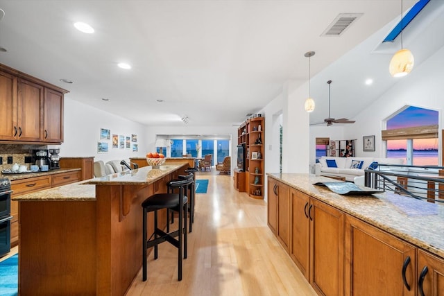 kitchen with a breakfast bar area, a kitchen island, pendant lighting, light stone countertops, and light hardwood / wood-style floors