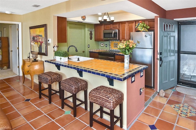 kitchen with sink, light tile patterned floors, a breakfast bar, appliances with stainless steel finishes, and tile countertops