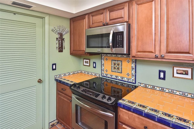 kitchen with tasteful backsplash, appliances with stainless steel finishes, and tile counters