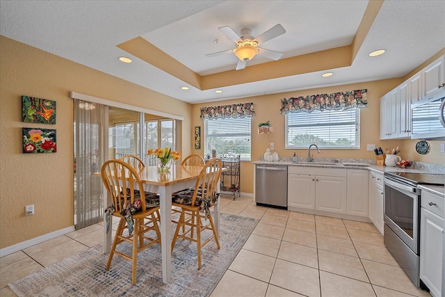 kitchen featuring sink, light tile patterned floors, appliances with stainless steel finishes, a raised ceiling, and white cabinets