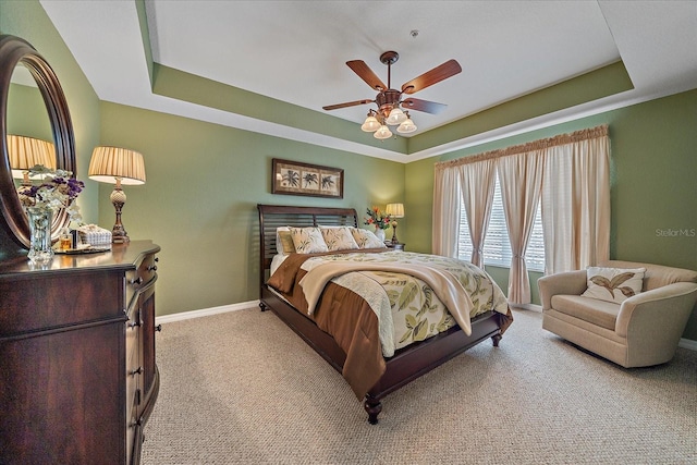 bedroom with ceiling fan, a tray ceiling, and light carpet