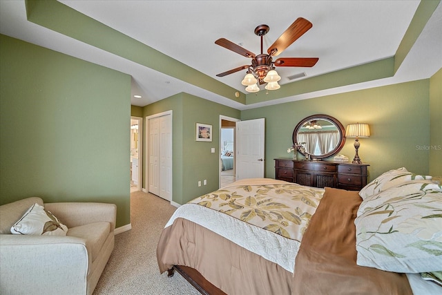 bedroom with light carpet, a tray ceiling, a closet, and ceiling fan