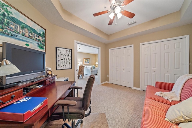 carpeted office with ceiling fan and a tray ceiling