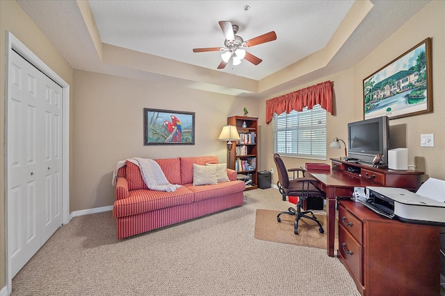 carpeted office space with a raised ceiling and ceiling fan