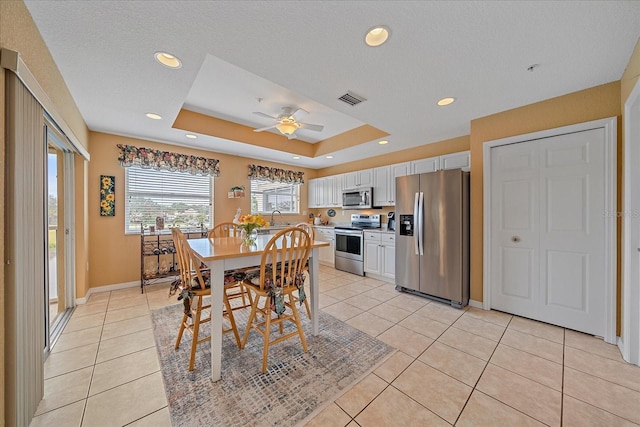 tiled dining space with a raised ceiling, ceiling fan, sink, and a textured ceiling