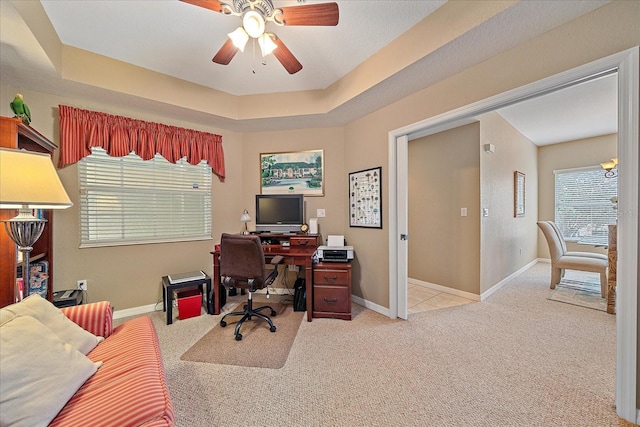 carpeted home office featuring a raised ceiling and ceiling fan