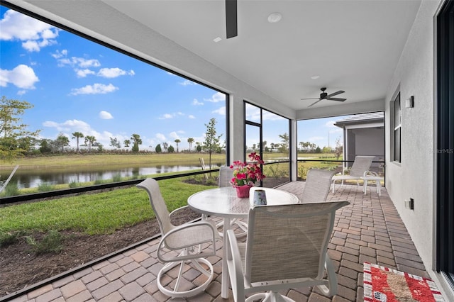 sunroom with ceiling fan and a water view