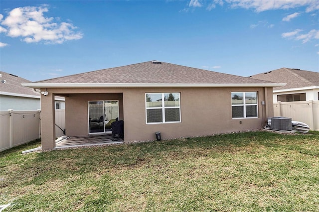 back of property with stucco siding, a fenced backyard, roof with shingles, and a yard